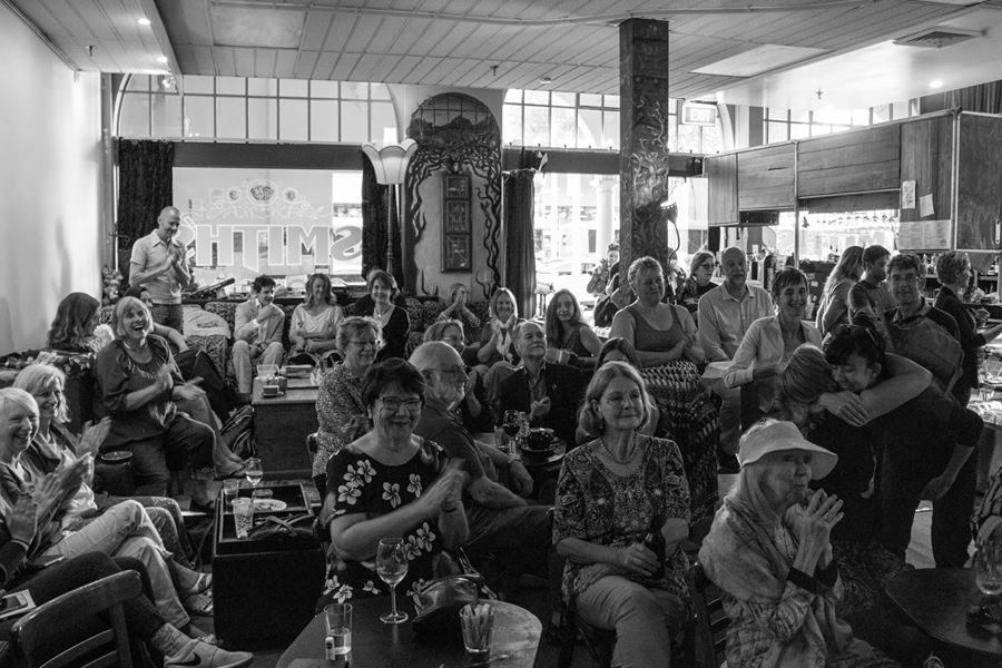 Photo of the audience at a Not Very Quiet event. The name of the venue, Smith's, can be seen in reverse on the window in the background.